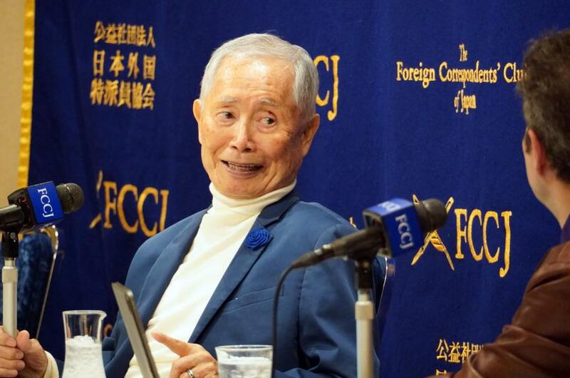George Takei speaks to reporters in front of a blue backdrop.