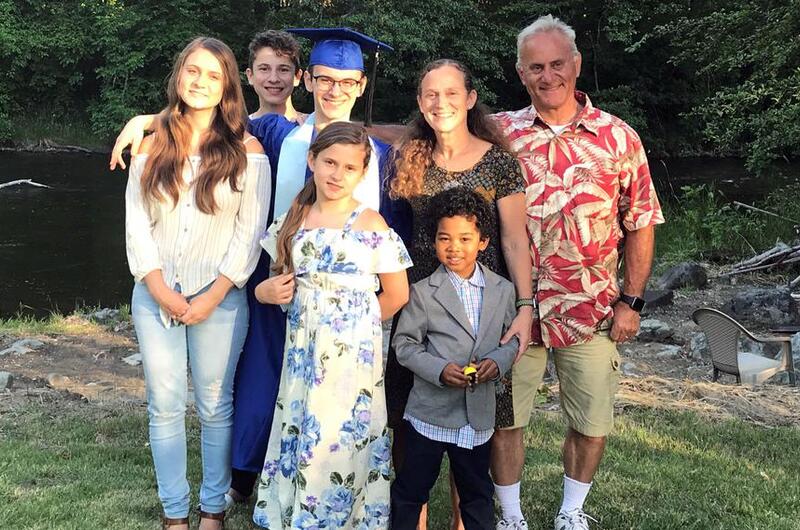 A family consisting of a father, mother and five children group together to pose on a grass lawn, with trees in the background.