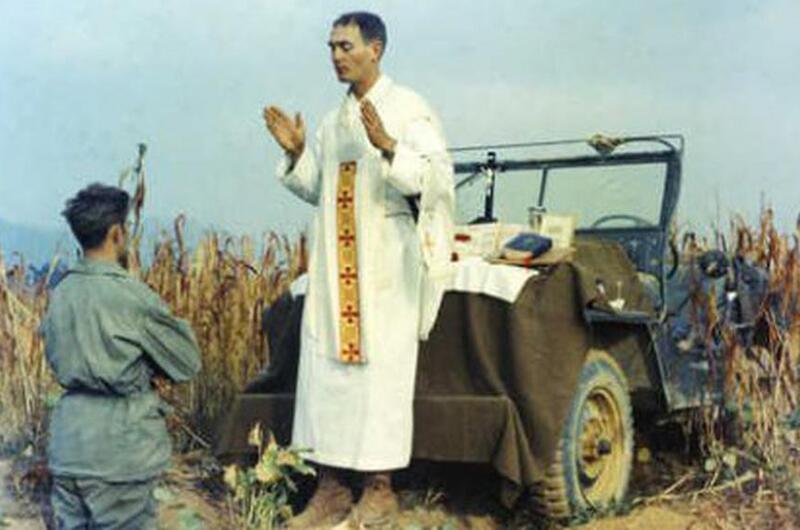 Kapaun stands above a soldier, with a jeep behind him.