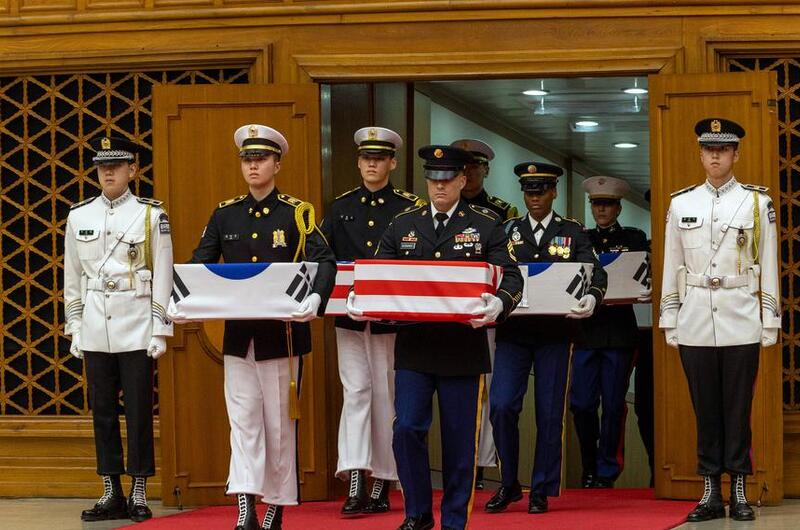 Service members in uniform hold boxes draped in Korean and American flags.