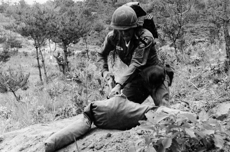 CHARGING A DUMMY representing the enemy during the intense testing, Sgt. Roger G. Cee of Salt Lake City, Utah, routs the "opponent" out of his foxhole. The sergeant tossed two grenades at the site before charging the make-believe enemy.