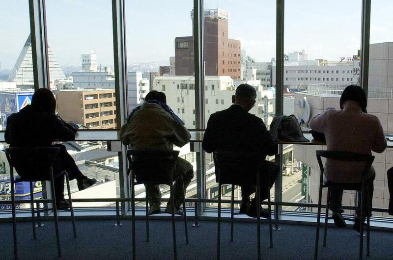 Four men seated in front of an all-glass wall/window that overlooks a cityscape.