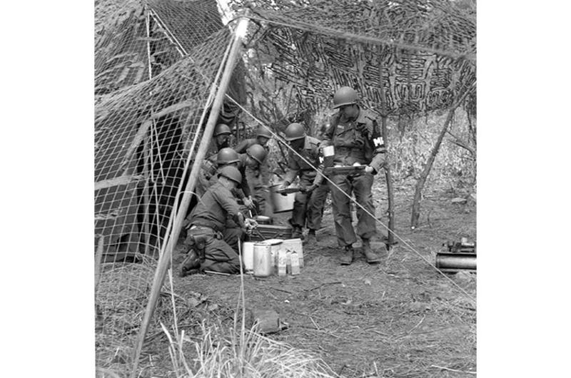 Group of MP's grabs a bite of chow, protected by camouflage netting, while on field assignment.