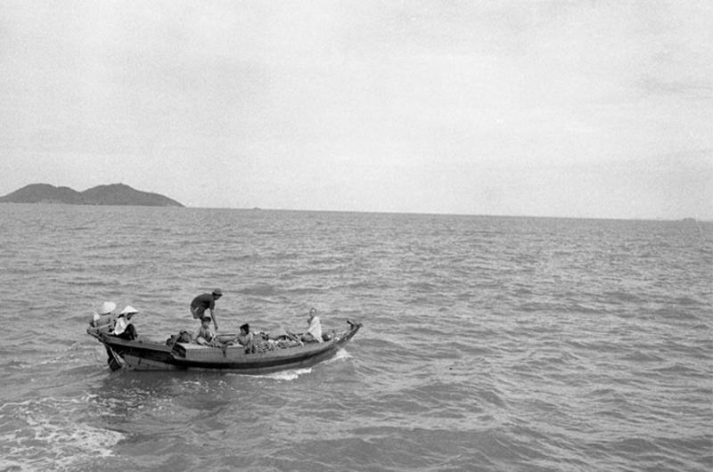 Swift boat stops sampan on way to market. Yellow-robed Buddhist monk sits in bow.