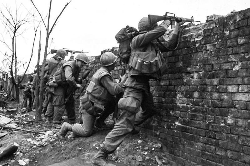 U.S. Marines take cover behind one of the bullet-riddled outer walls surrounding the Hue Citadel as they exchange fire with the enemy during the Tet Offensive.