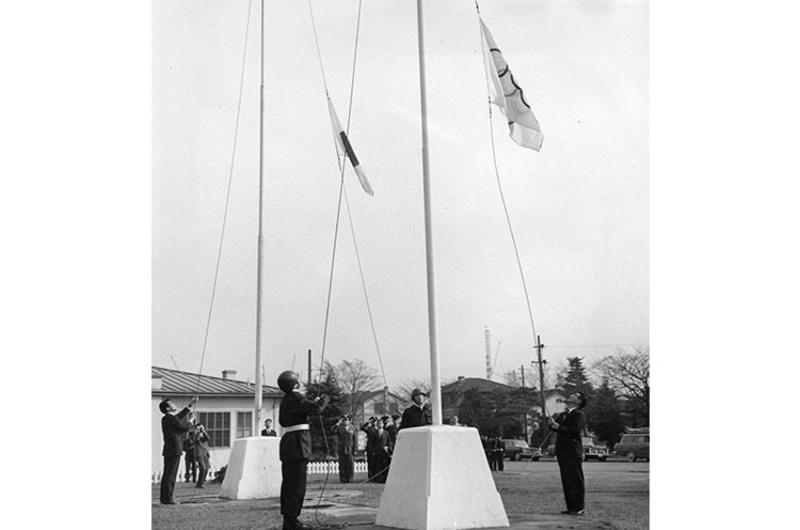 The five-ring Olympic flag and the Japanese national flag are raised at Washington Heights in Tokyo Tuesday.
