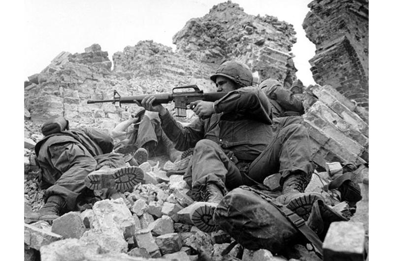 As a platoon leader and his radioman press into the rubble of the Dong Ba Tower for cover, a U.S. Marine fires back at a North Vietnamese sniper amid fighting in the Hue Citadel during the Tet Offensive.