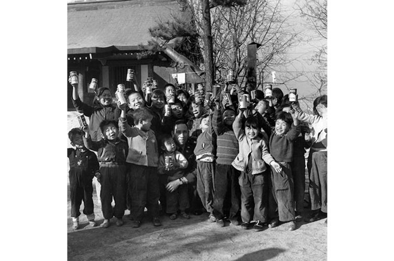 Cheers Go Up for Capt. Chavez as the orphans, holding canned soft drinks afloft, surrounded their benefactor, nearly hidden from view in the center, holding one of the smaller children from the orphanage.