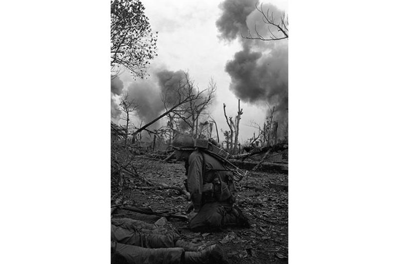 A cavalryman crouches down as smoke billows from North Vietnamese positions hit by artillery in the background.