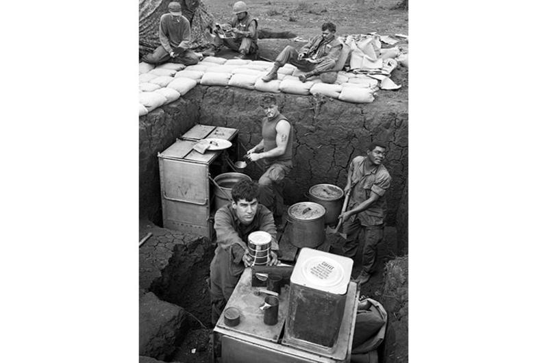 A Marine cooks soup while others either relax or work on better protecting a kitchen facility at the Khe Sanh base.