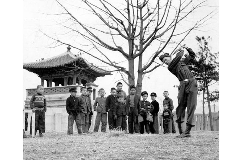 New ... To Koreans Anyway - Cpl. Dave Wagenvoord, Eight Army Forward Hq., shows a group of curious Korean youngsters how its done as he practices his golf game inside the capital grounds in Seoul.
