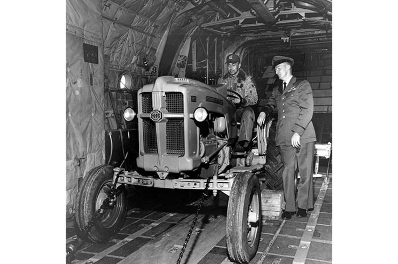 Capt. Simon (seated) and Capt. Whistler Inspect Tractor. Capt. Thomas Simon (seated) and Capt. John C. Whistler inspect a Minneapolis-Moline tractor in the belly of a C-130 plane.