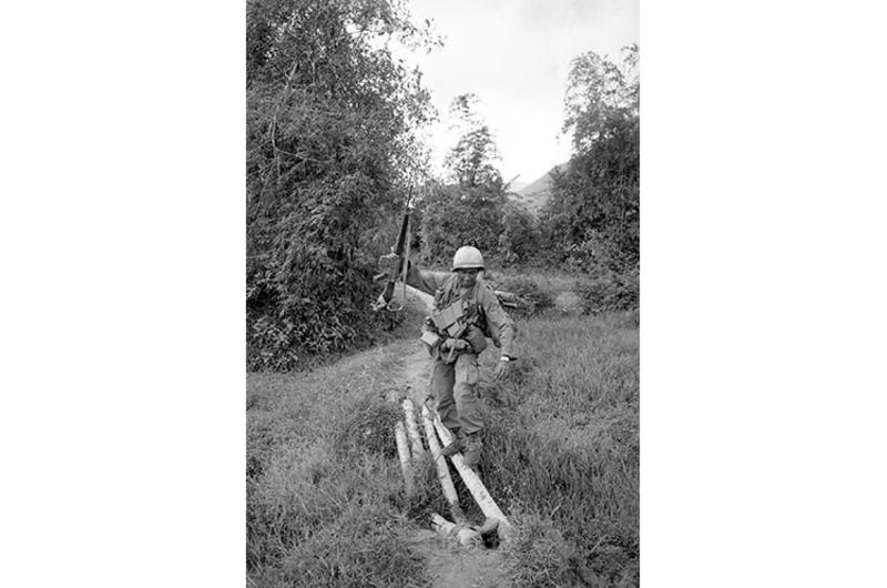 Infantrymen walk delicately over narrow bridge span.