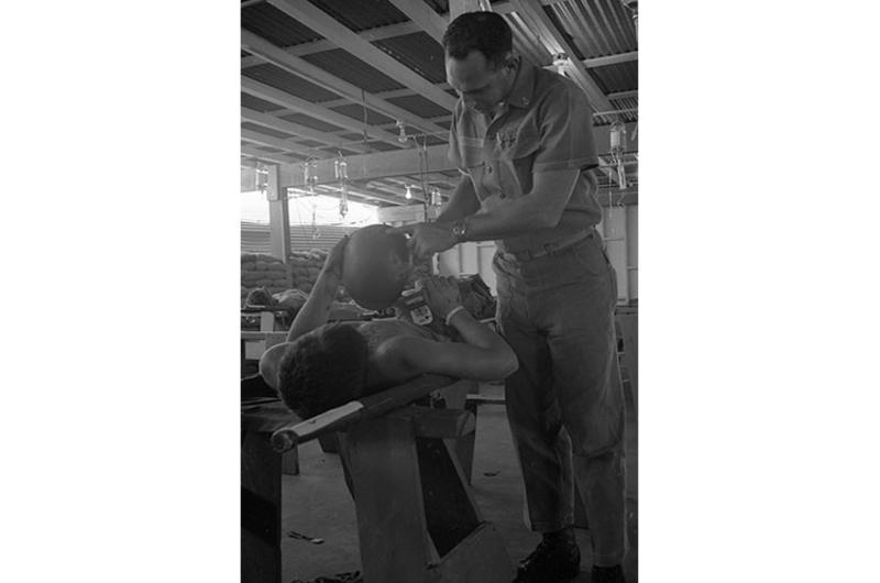 Patient whose helmet was riddled by schrapnel shows helmet to corpsman.