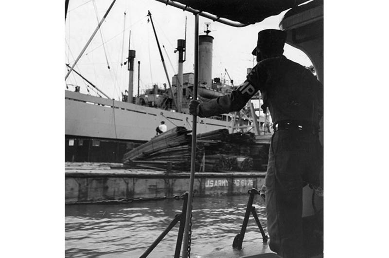 Freighter unloading in the harbor is checked by Army MP patrol, as are barges used to bring cargo ashore.