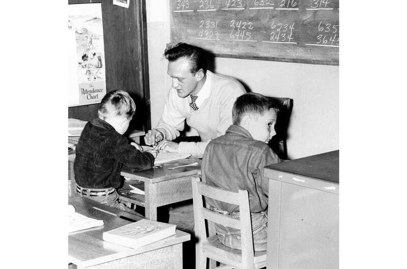 A black and white photo of a man sitting opposite a child at a desk.