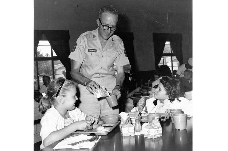 Sgt. 1st Class Bill Thompson pours milk for two students