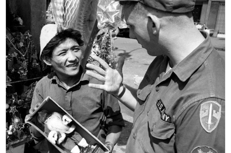 An American soldier engages in some friendly haggling with a Saigon street merchant over a Santa Claus figurine.