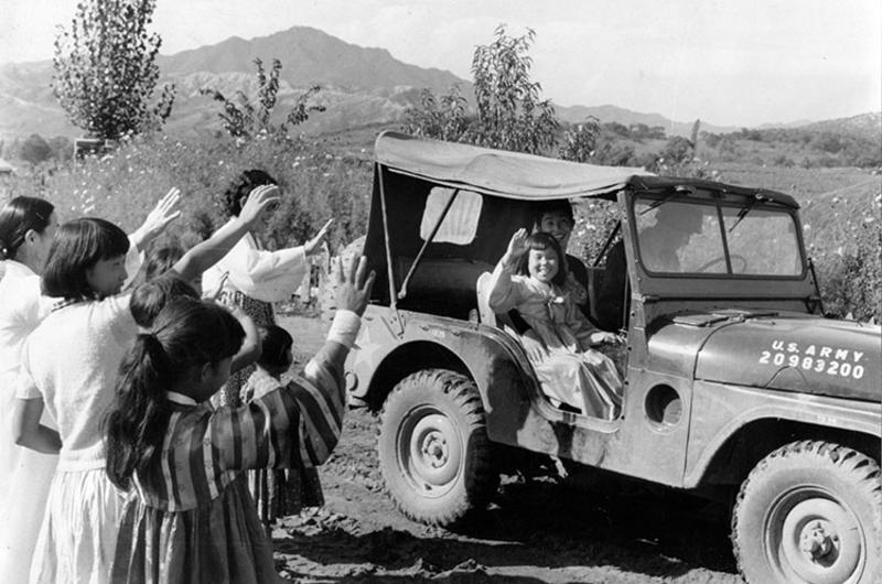 Happy orphan In Suk Han, 7, waves to her friends at the Hea Sung Orphanage as she leaves with Miss Elizabeth Lewis and an unidentified driver for a weekend in Seoul.