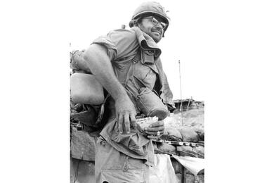 A vertical, black and white photo of a soldier smiling as he handles a bundle of mail.