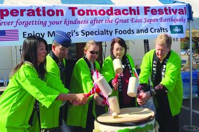 Five people in green Kimono-like robes beat a ceremonial barrel. 