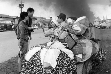 A fleeing Niigata family, whose home (near burning oil tanks in background) was destroyed, pauses to talk with Stars & Stripes reporter PFC Mike Mealey and photographer Masahiko Nakamura.