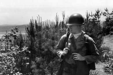 Lonely perimeter guard post is patrolled by PFC William E. Green on a hill near the division CP. When not playing, the band forms a security unit.