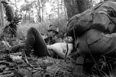 Soldier holds hand of wounded buddy and tries to comfort him as squad fights off 50 to 60 VC.