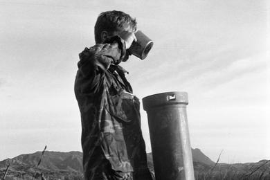 A Marine drinks from a field water pump, as other Marines behind him are busy digging in.