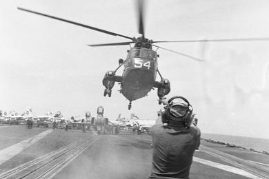 Dust whips up as a  member of the flight deck crew of the USS America signals as a lands on the air carriers flight deck.