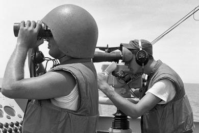 SK3 Samual W. Wade, left, air defense phone talker, and FTM3 Thomas G. Stone, TDT (Target Designation Transmitter), look into shore through binoculars on board USS Buchanan during Operation Sea Dragon.