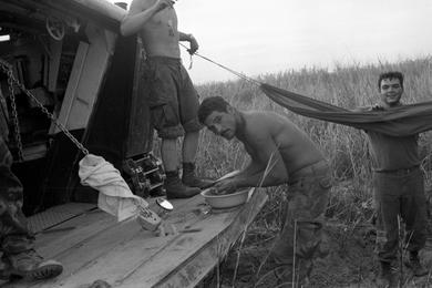 Lance Cpl. Nick Romano washes up as Company Commander Lanham Jr. hangs a captured hammock between two Amtracs (LTVs) with the help of another Marine.