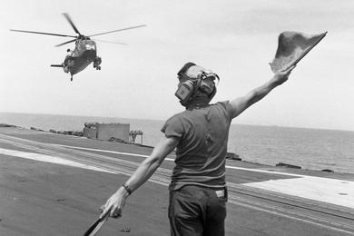 A member of the flight deck crew of the USS America signals to a helicopter approaching for a landing on the air carriers flight deck.