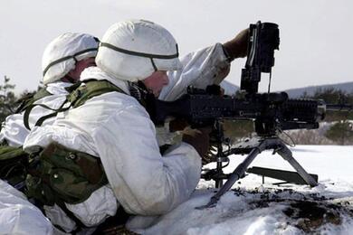Two soldiers handle a gun on snowy ground.
