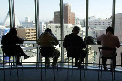 Four men seated in front of an all-glass wall/window that overlooks a cityscape.