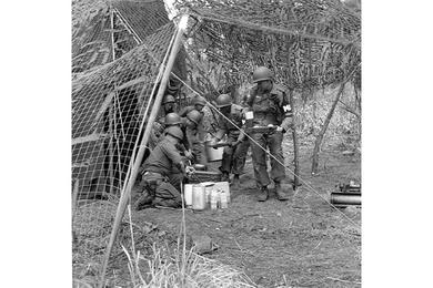 Group of MP's grabs a bite of chow, protected by camouflage netting, while on field assignment.