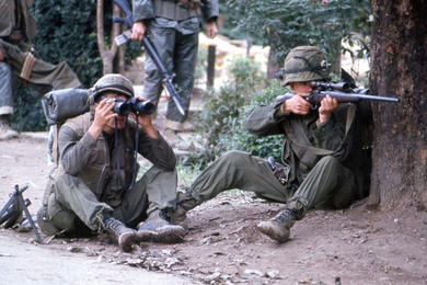 A Marine sniper takes aim from behind a tree as his comrade looks through a pair of binoculars to establish the enemy position in Hue during the battle for the city in 1968.