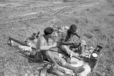 PFC Richard Villareal, left, and Lance Corp. K.D. Johnson Jr. of E Company, 2nd Battalion, 5th Marine Regiment, 1st Marine Division, relieved of their wet and muddy boots eat their C rations while in a blocking position 10 miles south of Da Nang.