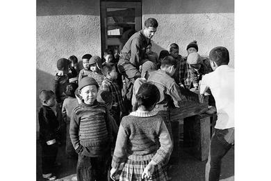 ORPHANS CLUSTER AROUND PFC SPERO METRAKOS AS HE SAWS WOOD FOR HOME'S STOVES