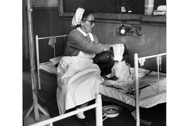 A German nurse attends to a small child in a bed on one of the wards at the West German Red Cross Hospital.