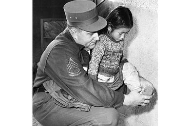 TINY MISS IS HELPED WITH SHOE BY SFC LEROY HALL