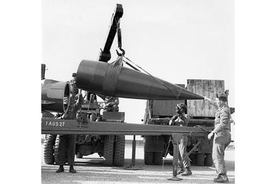 Members of a missile battery of the 4th U.S. Missile Command load the warhead of an Honest John missile onto its launch pad with the help of a crane.