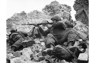 As his platoon leader and a radio operator press into the rubble for cover, a U.S. Marine fires back at a North Vietnamese sniper during fighting in the Citadel at Hue.