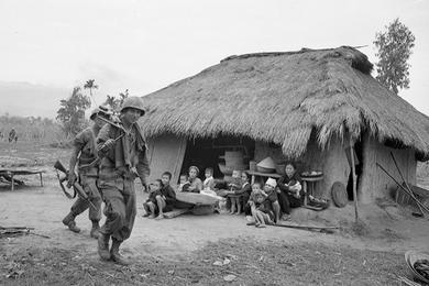 Local Vietnamese look on as cavalrymen on patrol pass through their village.