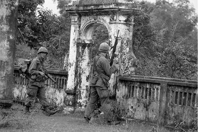 Two cavalrymen pass an ancient stone gate.