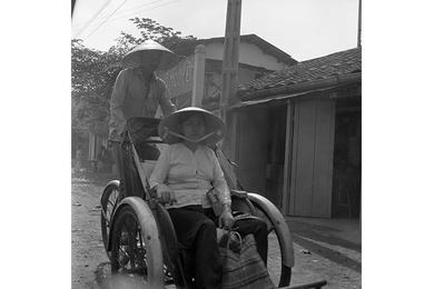 Vietnamese women is ridden around in the streets in a rickshaw, location unknown.