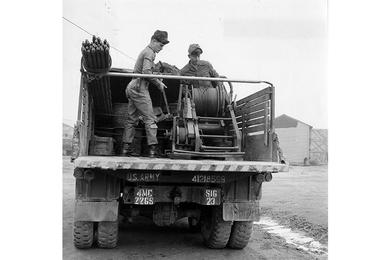 Ground cable for communication between units in field is laid by Pvt. Bill Schnoering (left) and his buddy, PFC Roy Huddleston.