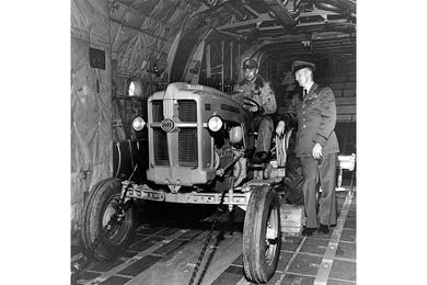 Capt. Simon (seated) and Capt. Whistler Inspect Tractor. Capt. Thomas Simon (seated) and Capt. John C. Whistler inspect a Minneapolis-Moline tractor in the belly of a C-130 plane.