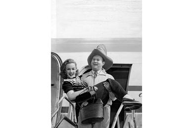 PRETTY BUNDLE -  Johnny Grant, USO troupe emcee, carries petite Piper Laurie from their Pan American Clipper at Tokyo 's International airport.