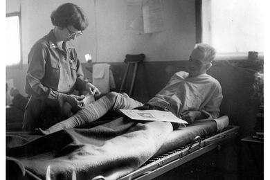 CAPT. BROWN ADJUSTS BANDAGE Attention at Quonset Hut Hospital. Capt. Brown, one of the nurses at the quonset hut hospital adjecent to the 54th Medical Detachment air ambulance helicopter field, adjust the leg bandage of a wounded soldier.